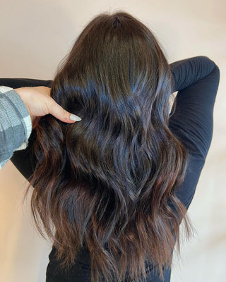 A dark-haired woman in Glam Seamless chocolate dipped color hair, with her hands on her head posing.