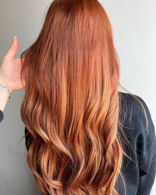 The back of a woman's head shows her hair, which features warm, rich shades of orange with hints of brown and red in the hair extensions.