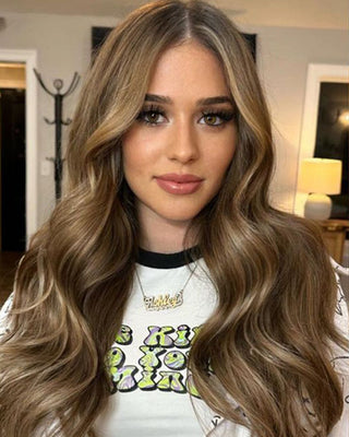 A woman with long hair is wearing a t-shirt. She is showcasing the Glam Seamless rooted caramel hair extension color.