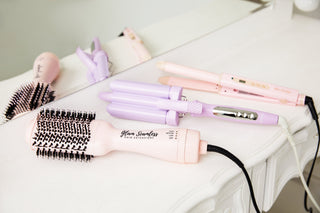 Hair dryer, curling iron, and brush neatly arranged on a white table. 